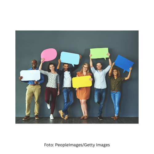 ein Foto mit mehreren Personen. Sie haltenbunte Sprechblasen aus Karton hoch