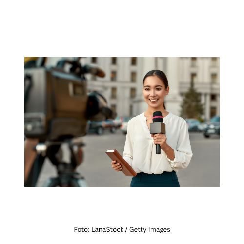 Eine Reporterin auf einer Straße mit einem Mikrofon in der Hand. Sie spricht in eine Kamera.